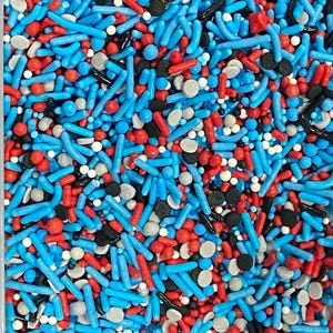May include: A close-up shot of a mix of colorful sprinkles. The sprinkles include blue jimmies, red rods, black and gray round sprinkles, and white nonpareils. These sprinkles are perfect for decorating cakes, cupcakes, and other baked goods.