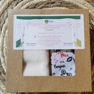 Puede incluir: Una caja de cartón marrón con una etiqueta blanca que dice "Kit DIY Lingettes lavables" y "5 lingettes". La caja contiene dos paños blancos, uno con la palabra "Paris" y el otro con la palabra "Bonjour".