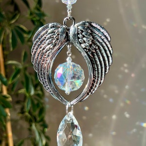 May include: A silver angel wing crystal suncatcher with a clear crystal teardrop and a round crystal prism. The suncatcher is hanging from a chain with clear crystal beads.