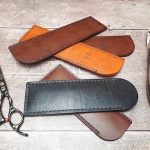 May include: Four leather cases for grooming tools, including scissors and clippers. The cases are brown, black, and orange, and have the words "Cudo", "D.S", and "J.E.S.V" embossed on them.