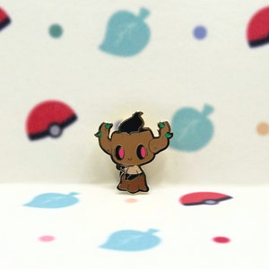 Puede incluir: Un pin de esmalte dorado con un personaje de dibujos animados con piel marrón, un cuerpo de tronco de árbol marrón, hojas verdes y ojos rosas. El personaje sonríe y tiene un mechón de pelo negro en la cabeza.