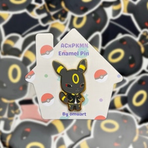 Puede incluir: Un pin de esmalte negro y amarillo con una versión de dibujos animados del Pokémon Umbreon. El pin está en una tarjeta blanca con el texto "ACxPKMN Enamel Pin" y "By omuart".