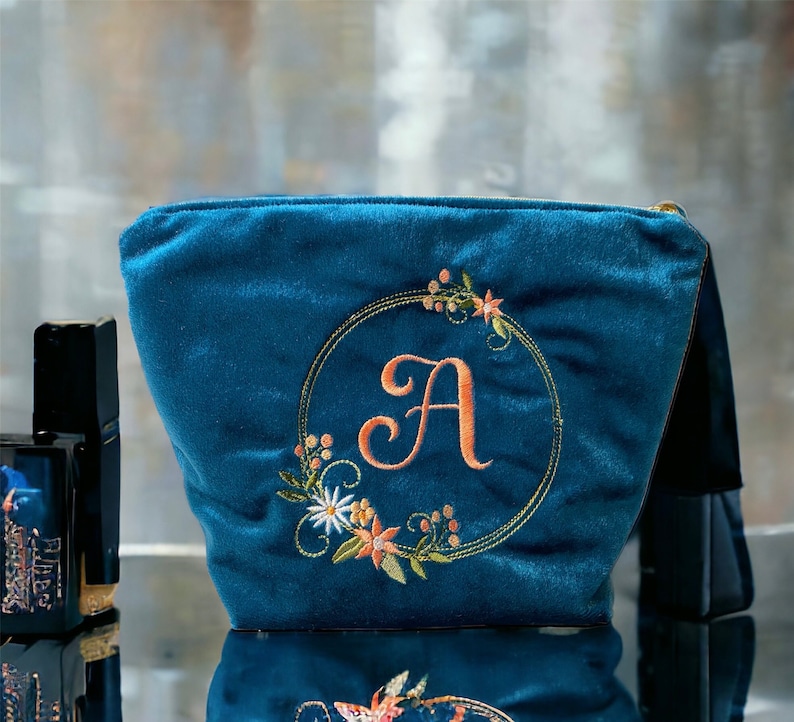 A teal blue velvet makeup bag with embroidery and an initial on it