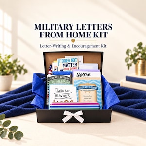May include: A black gift box containing a military letters from home kit, filled with various greeting cards, stationery, and a striped pencil case. The box is lined with blue tissue paper and features a white ribbon bow on the front exterior.