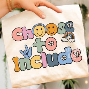 May include: Cream-colored t-shirt with the phrase "Choose to Include" in a colorful, retro font. The design includes smiley faces, a rainbow, and a hand gesture, creating a cheerful and inclusive vibe.