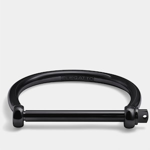 以下が含まれることがあります： D字型のデザインの黒いブレスレット。ブレスレットはネジのような留め具があり、上部には「ELEGATTO」の文字が刻まれています。ブレスレットは光沢のある黒色の無垢材で作られています。