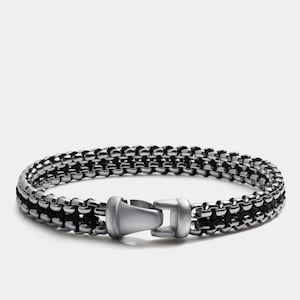 May include: A silver chain bracelet with a black cord woven through it. The bracelet has a silver clasp with the word "SEACRAFT" engraved on it.