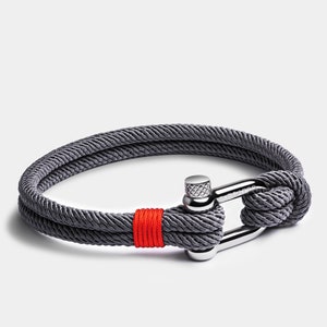 May include: A gray rope bracelet with a silver clasp and a red accent. The clasp has the word "LIVACAO" engraved on it.