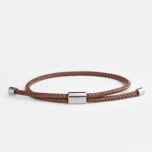 May include: A brown braided cord bracelet with silver metal ends and a silver metal clasp that says "ELEGATTO".