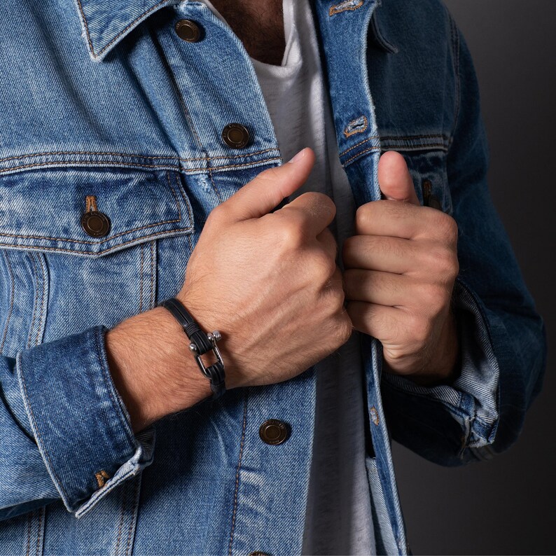 May include: A black leather bracelet with a silver clasp. The bracelet is worn on the wrist of a person wearing a denim jacket.