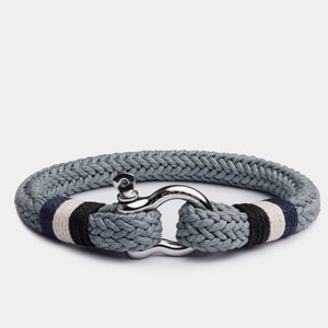 May include: A gray rope bracelet with a silver clasp. The rope has white and black stripes.
