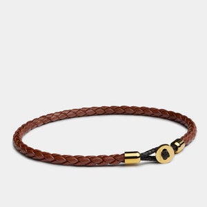 May include: A brown leather braided bracelet with gold accents and a black cord closure.