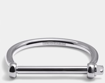 May include: A silver metal bracelet with a simple design. The bracelet has a straight bar that goes through a curved loop. The bracelet is engraved with the word "ELEGATTO".