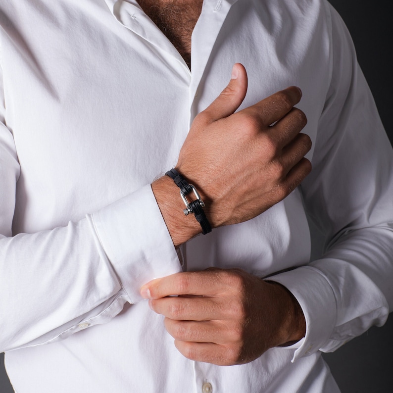 May include: A black leather bracelet with a silver clasp. The bracelet is worn on a person's wrist.