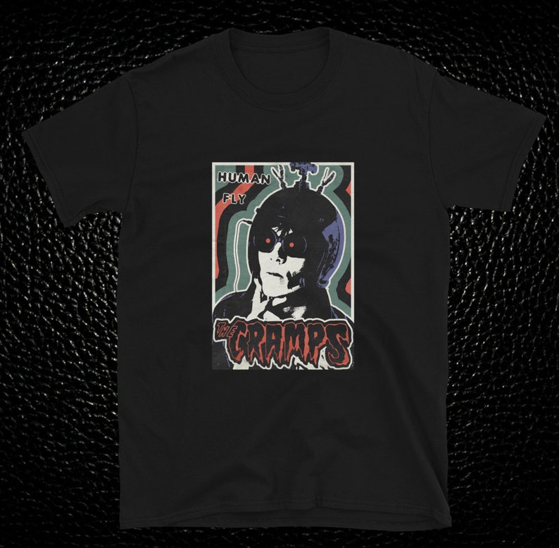 May include: Black t-shirt with a vintage-style graphic of a person wearing a helmet with the text "Human Fly" and the band name "The Cramps" in red and black lettering.