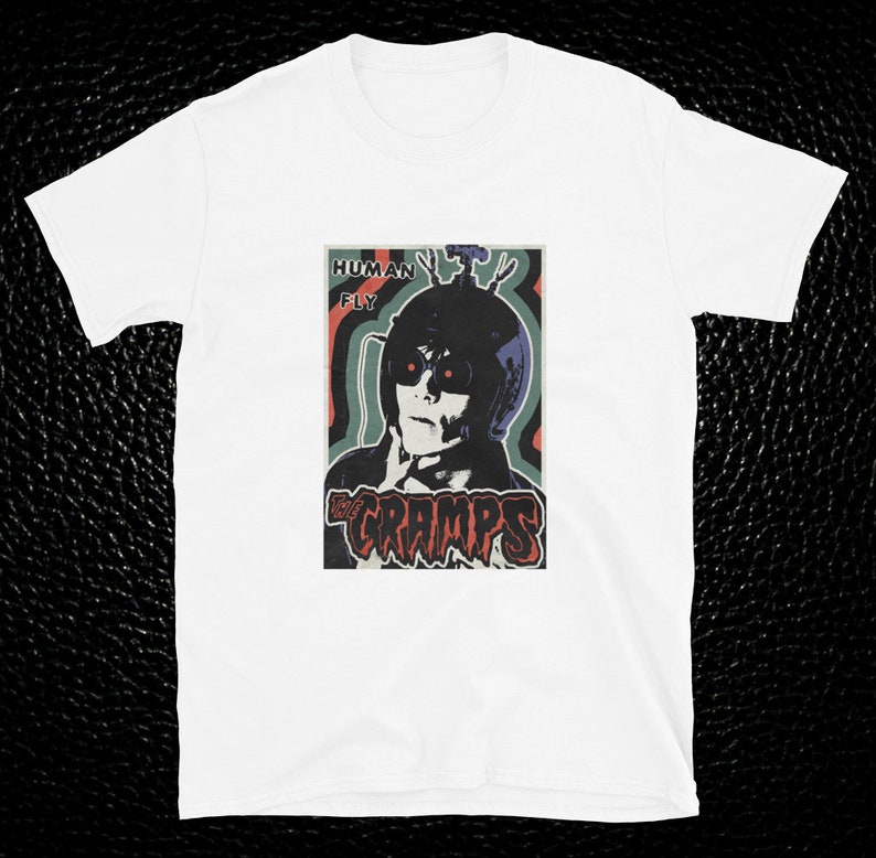 May include: White t-shirt with a vintage-style graphic of a person wearing a helmet and goggles with the text "Human Fly" and "The Cramps" printed on the front.