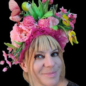 May include: A pink and green floral crown with a butterfly and a ladybug. The crown is made of silk flowers and has a delicate, feminine feel.