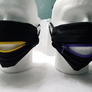 May include: Two black face masks with a zipper sewn into the mouth area. One mask has a yellow zipper and the other has a purple zipper.