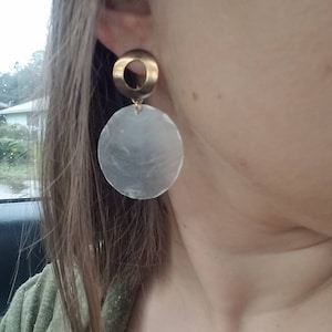 May include: Gold and white circle earrings. The earrings have a gold ring with a white circle pendant.