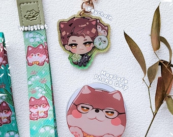 May include: A Valko Bulky Set featuring a green wristlet with a repeating cat pattern, a star-shaped keychain with an illustrated character, and a round MagSafe phone grip displaying a brown cat wearing glasses and a yellow bow tie.