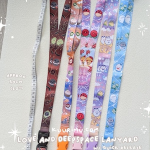 May include: Five fabric lanyards with quick-release buckles, each featuring distinct cartoon character prints in brown, orange, pink, purple, and blue. A measuring tape is visible, indicating a length of approximately 50 cm or 20 inches.