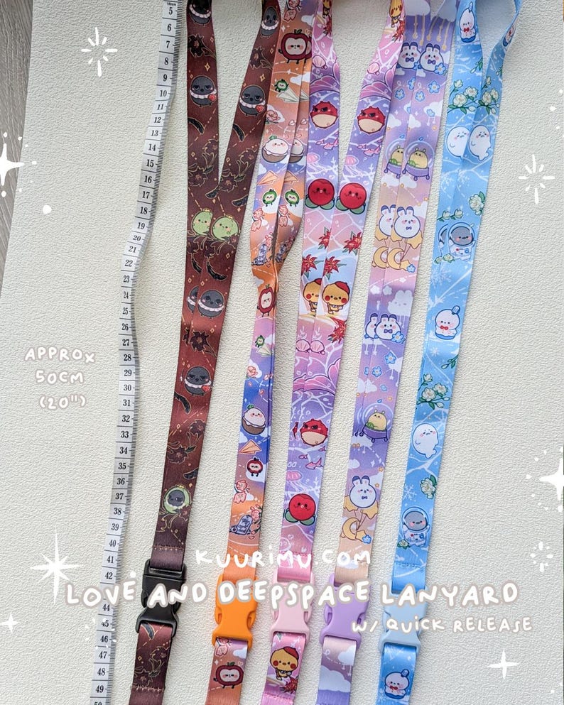 May include: Five fabric lanyards with quick-release buckles, each featuring distinct cartoon character prints in brown, orange, pink, purple, and blue. A measuring tape is visible, indicating a length of approximately 50 cm or 20 inches.