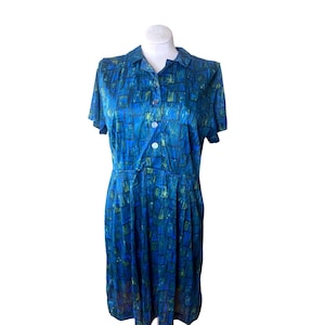 May include: A vintage blue dress with a collared neckline and short sleeves. The dress features a pattern of blue and green squares and is buttoned down the front. The dress is displayed on a white mannequin.