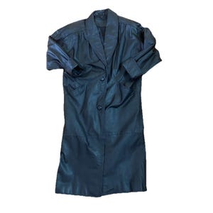 May include: A black leather coat with a notched collar and two button closure. The coat has long sleeves with folded cuffs and two front pockets. The coat is knee-length and appears to be vintage.