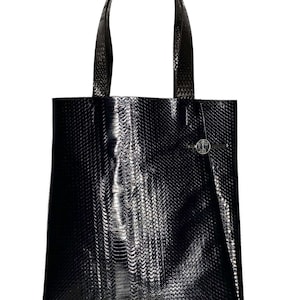Może przedstawiać: Czarna skórzana torba typu tote ze wzorem skóry węża. Torba ma jeden górny uchwyt i mały srebrny akcent z przodu.