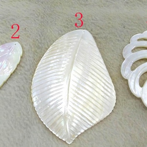 May include: Four white mother of pearl shell leaf shapes with different designs. The leaves are numbered 1 through 4.