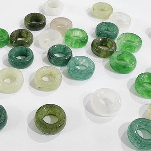 May include: A collection of green, white, and cream colored jade rings. The rings are all different sizes and shapes, and some have a marbled pattern.
