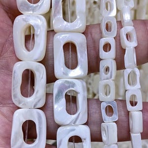 May include: A strand of white shell beads with square shapes and oval holes. The beads are strung on a clear elastic cord.