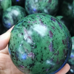 May include: A green and pink zoisite sphere with a speckled pattern. The sphere is smooth and polished.