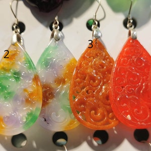 Könnte beinhalten: Fünf Paare Hängeohrringe mit aufwendigen geschnitzten Designs. Die Ohrringe sind aus verschiedenen Steinfarben gefertigt, darunter Lila, Grün, Weiß, Orange, Rot und Pink.