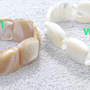 May include: Two shell bracelets, one brown and one white. The bracelets are made of rectangular shell pieces.