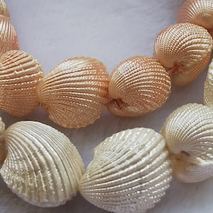 Könnte beinhalten: Eine Kette aus weißen und pfirsichfarbenen Muscheln, die in einem Kreis angeordnet sind. Die Muscheln sind glatt und haben einen Perlmuttglanz.
