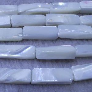 Może przedstawiać: Szereg białych, prostokątnych, iryzujących koralików z muszli. Korale mają gładkie, polerowane wykończenie i subtelny połysk.