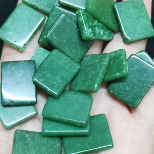 Könnte beinhalten: Eine Sammlung grüner Jade-Quadrate, jedes mit einem leicht anderen Grünton. Die Steine sind glatt und poliert und haben ein natürliches, organisches Aussehen.