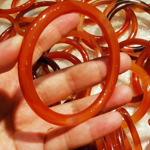 Puede incluir: Un montón de pulseras de cornalina roja. Las pulseras están hechas de piedra lisa y pulida y tienen un aspecto natural y terroso.