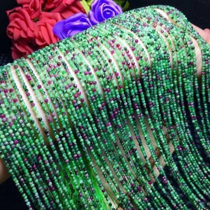 Puede incluir: Una hebra de cuentas de piedras preciosas verdes y rojas. Las cuentas son pequeñas y redondas, y están enhebradas en un alambre fino. La hebra es larga y fluida, y es perfecta para hacer joyas.