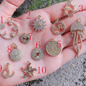 May include: Ten gold-tone charms with various designs, including a sun, a heart, a star, a moon, a jellyfish, a coin, and a hand. The charms are decorated with clear rhinestones and some have colourful accents.