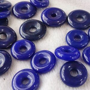 Puede incluir: Una colecci&oacute;n de 18 cuentas azules en forma de rosquilla con un agujero en el centro. Las cuentas est&aacute;n hechas de un material liso y brillante.