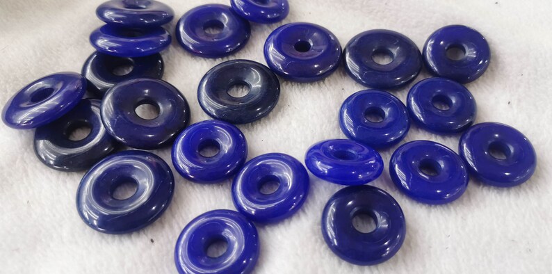 Puede incluir: Una colecci&oacute;n de 18 cuentas azules en forma de rosquilla con un agujero en el centro. Las cuentas est&aacute;n hechas de un material liso y brillante.