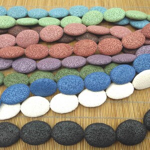 May include: A selection of oval lava rock beads in shades of blue, green, purple, and black. The beads have a textured surface and are strung together. These beads are likely for jewellery making or other craft projects.
