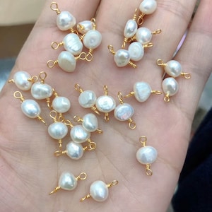 Puede incluir: Una colección de perlas de agua dulce blancas con lazos de alambre dorado. Las perlas son de varias formas y tamaños, y algunas tienen un ligero brillo iridiscente.