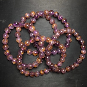 May include: A set of four amethyst bracelets with gold inclusions. The bracelets are made of round beads and are stacked on top of each other.