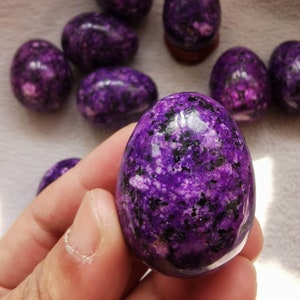 May include: A collection of purple and black speckled crystal eggs. The eggs are smooth and polished, with a variety of sizes and shapes.