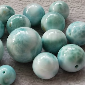 Puede incluir: Una colección de cuentas redondas de jaspe oceánico, de color azul y blanco, con un aspecto de espuma de mar. Las cuentas son lisas y pulidas.