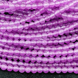 Può includere: Primo piano di una collezione di piccole perline rotonde di colore viola chiaro. Le perline sono infilate insieme, creando un aspetto stratificato e strutturato. Le perline sono di dimensioni e colore uniformi, con una qualità leggermente traslucida.