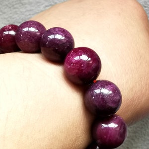Puede incluir: Un brazalete hecho de cuentas de piedras preciosas de color púrpura oscuro. Las cuentas son redondas y lisas, y tienen un ligero brillo.